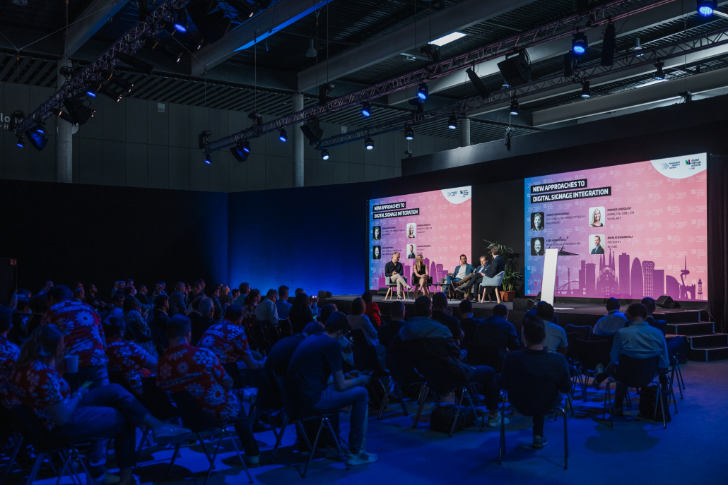 Zoomed out image of crowd watching a group talk about digital signage on stage